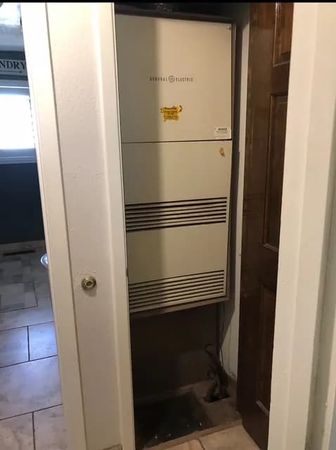 Older furnace in a narrow utility closet before replacement by Cyclone Air Systems